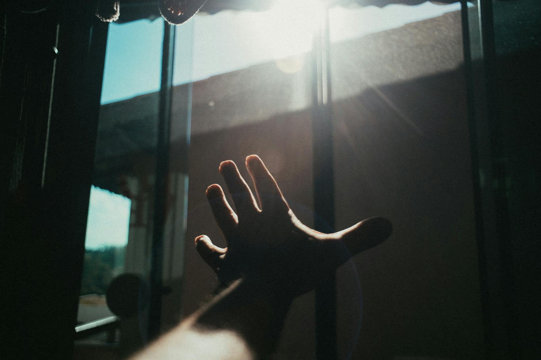 Person sitting alone by a window looking thoughtful, with soft natural lighting suggesting hope